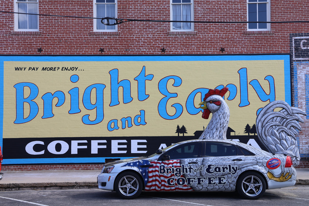 Car with a rooster design and 'Bright and Early Coffee' branding in front of a mural. in hico texas
